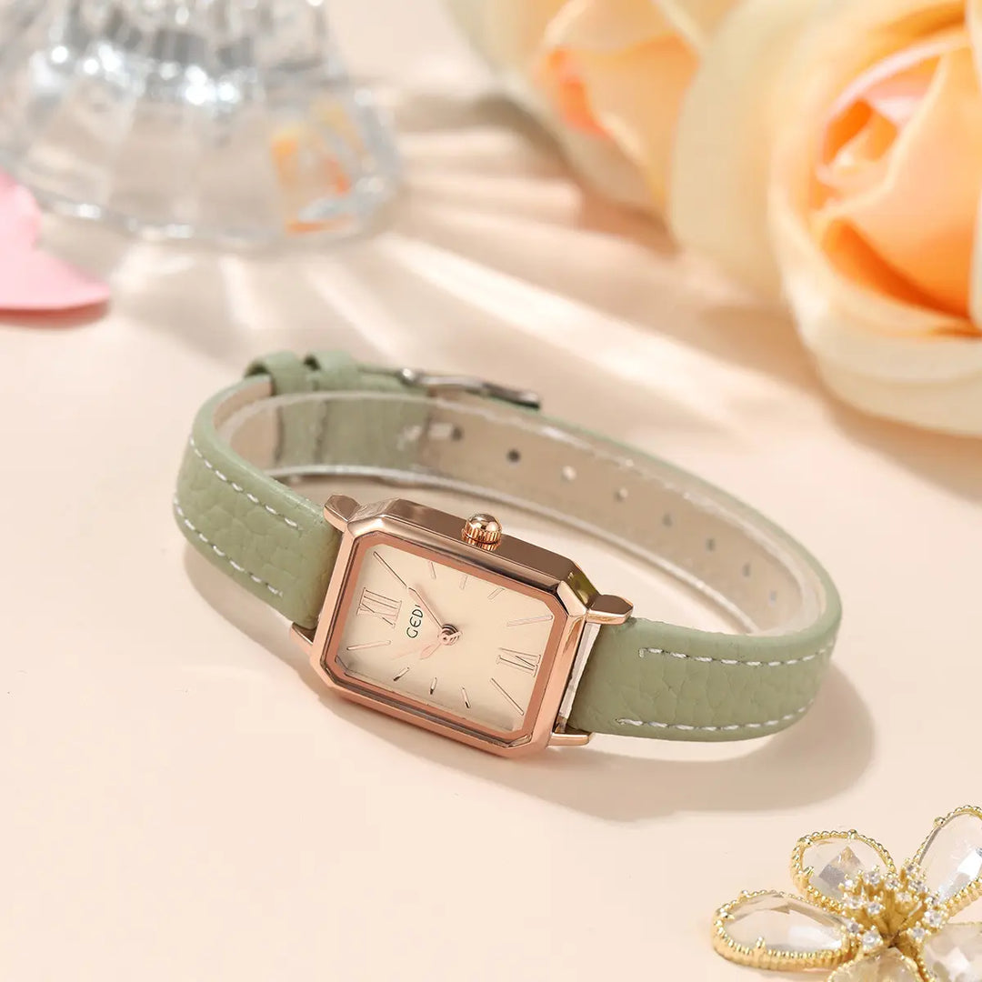 Elegant rose gold rectangular watch with a pale green dial and faux leather strap featuring white contrast stitching, shown at an angle on a soft neutral surface.