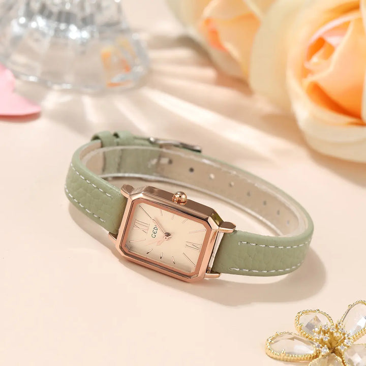 Elegant rose gold rectangular watch with a pale green dial and faux leather strap featuring white contrast stitching, shown at an angle on a soft neutral surface.
