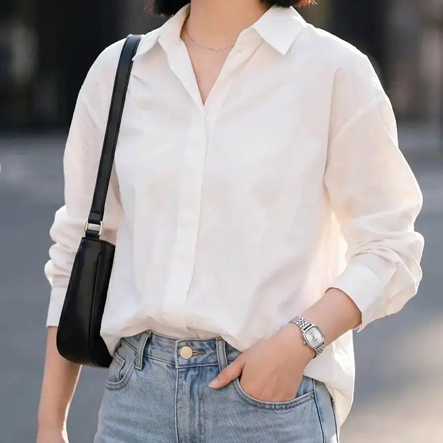 A woman wearing a silver Gedi quartz watch with a square-cushion case and a multi-link stainless steel bracelet, styled with a white shirt and jeans in an urban setting.