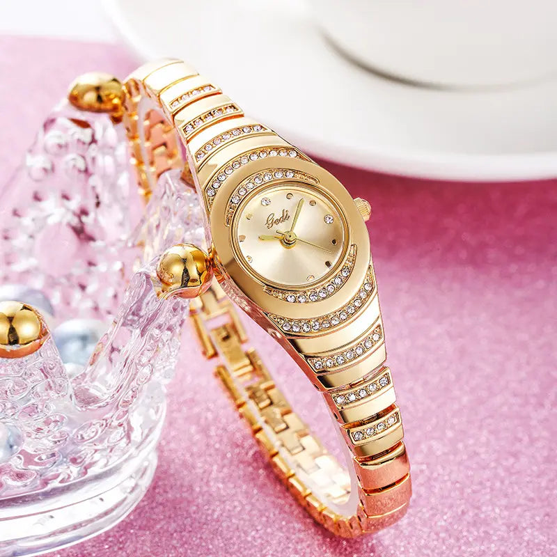 Elegant gold-tone women's bracelet watch with shimmering crystal embellishments on the bezel and integrated links, displayed in a studio setting with soft lighting.