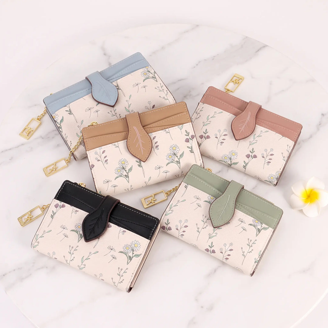 Collection of Gorik chic floral bi-fold wallets in various colors including blue, tan, pink, black, and sage green, showcasing their delicate floral print and leaf-shaped tab closure.