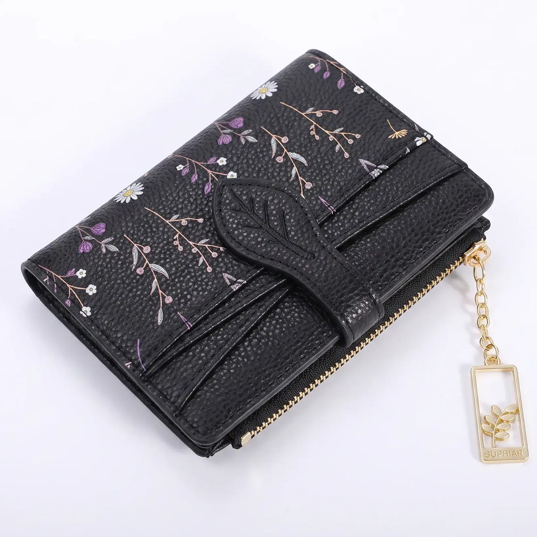 Gorik bi-fold wallet in Midnight Black floral print, featuring a contrasting black flap with a leaf-shaped closure and gold-tone hardware. This compact women's wallet includes a zippered coin pocket on the back and a dangling floral charm.