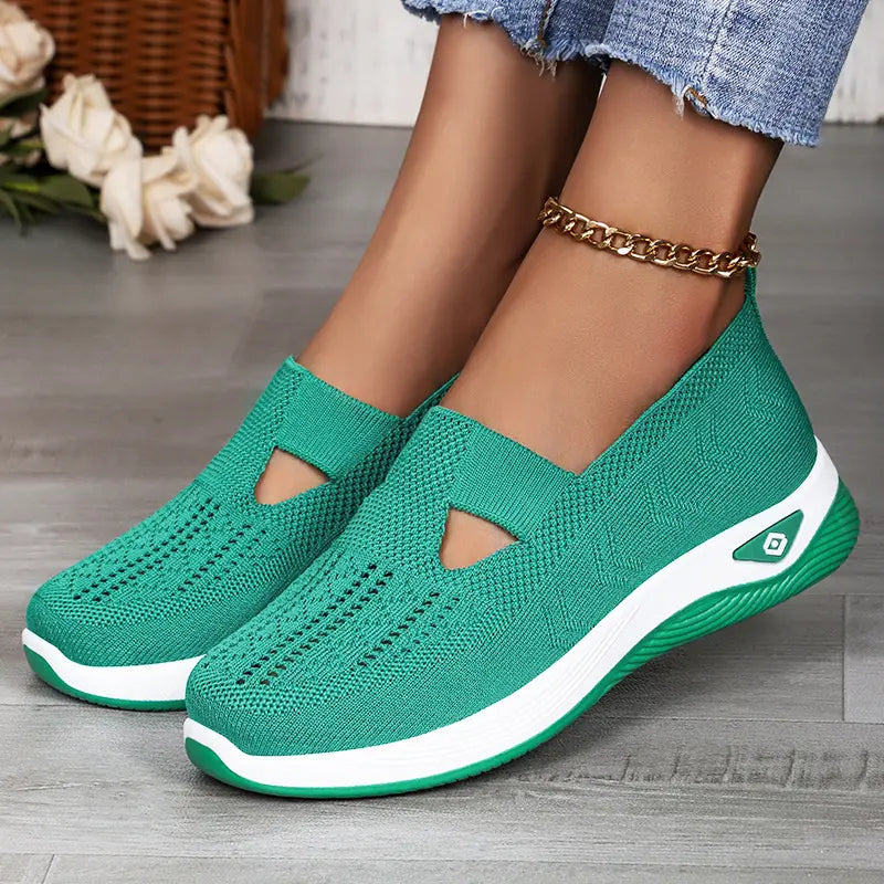 A pair of green breathable knit slip-on sneakers worn by a woman, showcasing their casual style and comfortable fit with a visible geometric weave pattern and white sole.