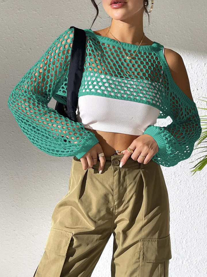 Green crochet crop top with cold-shoulder design and voluminous sleeves, worn by a model with a white underlayer and khaki cargo pants.