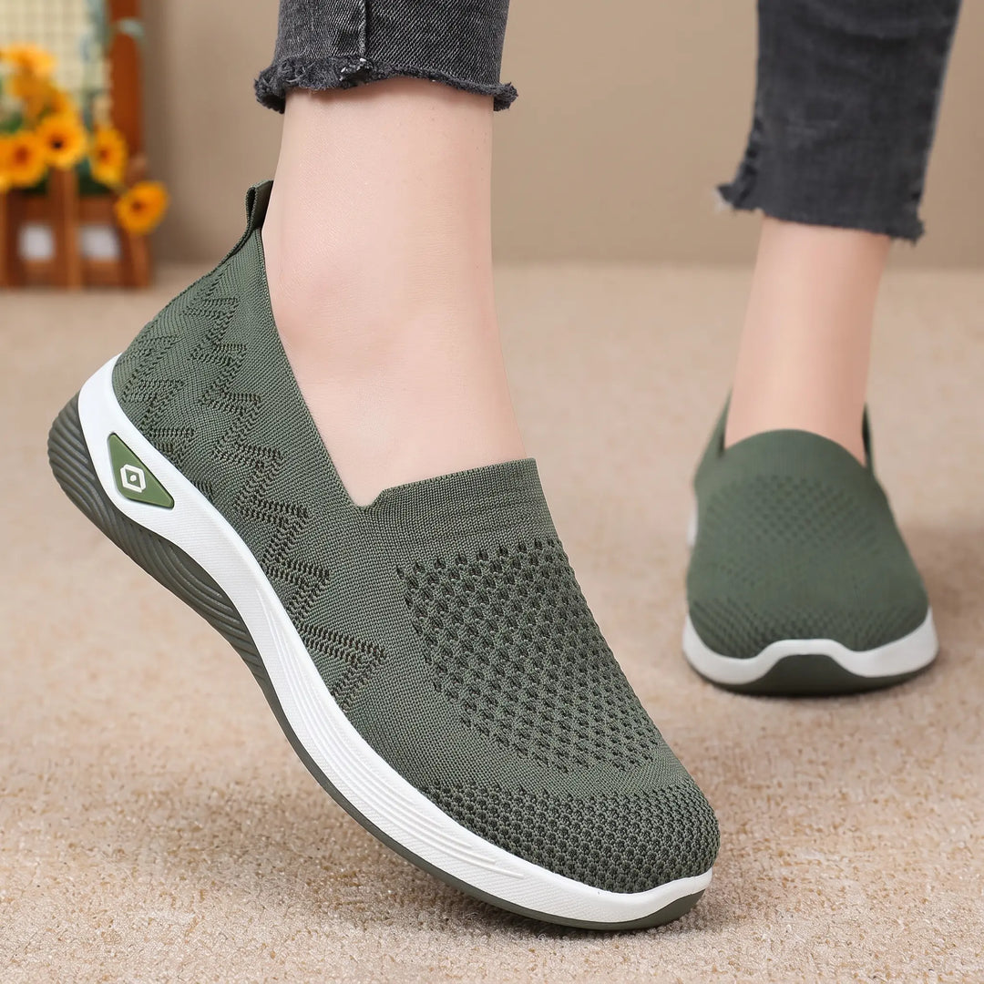 Green breathable knit slip-on sneakers with diamond and chevron patterns, worn by a person with grey jeans, showcasing the comfortable fit and white sculpted sole.