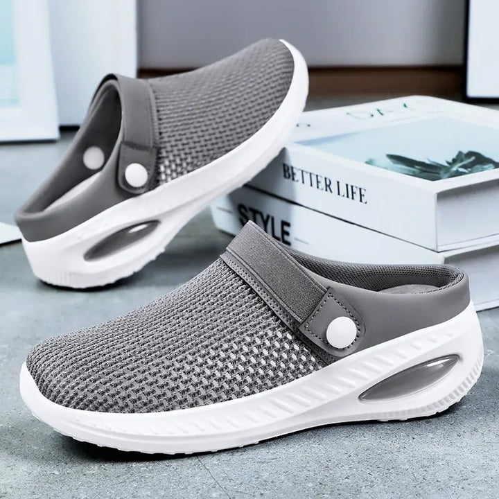 Grey breathable mesh slip-on clogs with white air cushion sole and adjustable strap, shown in a three-quarter view on a studio background with books.