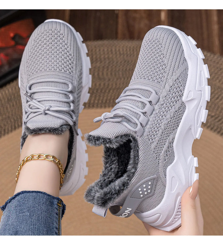Close-up lifestyle view of grey knit ankle boots with plush faux fur lining and chunky white platform soles, shown on a model wearing denim and a gold bracelet.