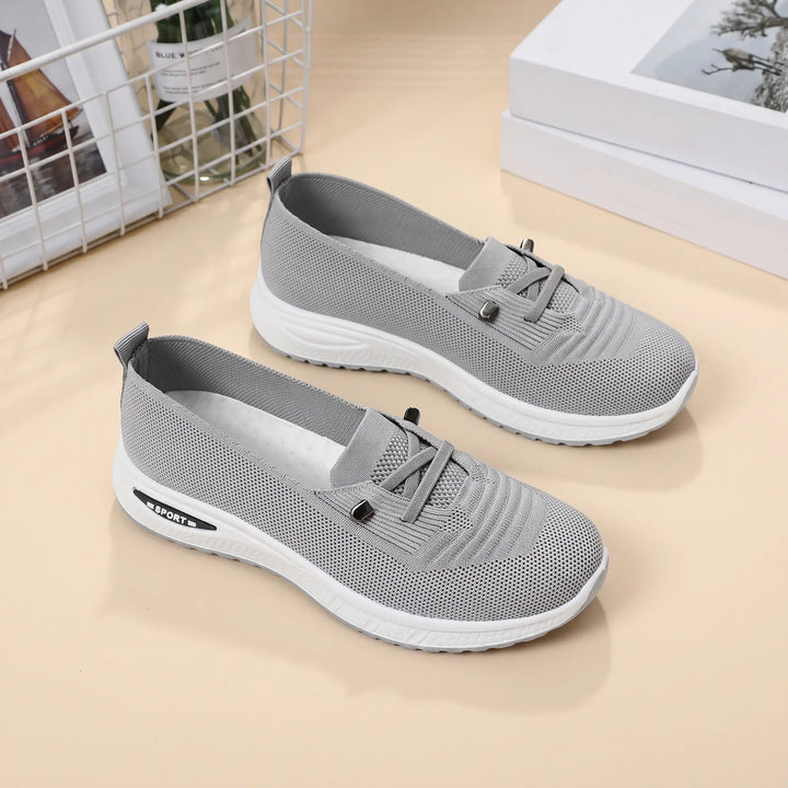 Pair of grey breathable knit mesh slip-on sneakers with decorative white lacing and a white EVA midsole with &
