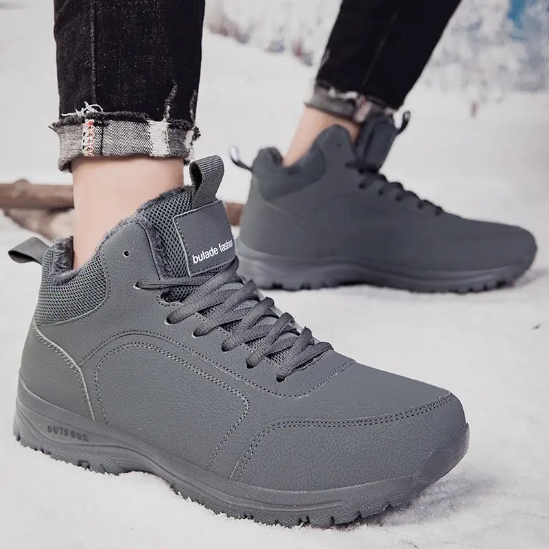 Grey men's mid-top winter boots with faux fur lining, worn by a model in a snowy outdoor setting, featuring lace-up closure and rugged soles.