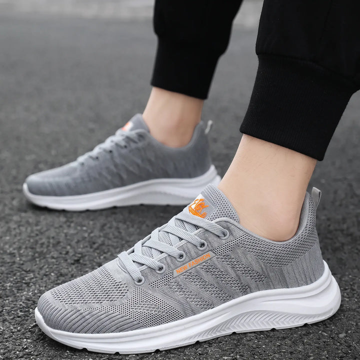 A pair of grey breathable mesh trainers with white soles worn by a person on a street, showcasing their lightweight, casual style.