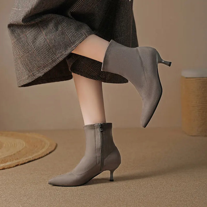 Grey suede-like stretch ankle boots with pointed toe and stiletto heel, worn with a plaid skirt.