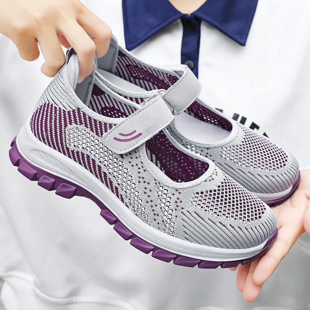 Pair of light grey and purple engineered knit walking shoes with a hook-and-loop strap, presented from a three-quarter angle against a studio background.