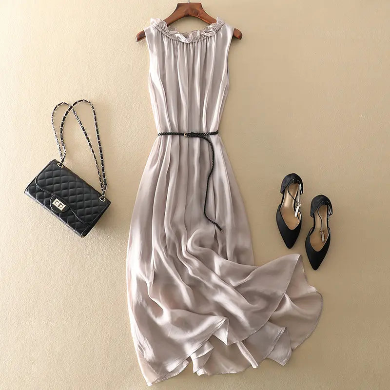 Muted grey pure silk midi slip dress laid flat with a black quilted handbag and black heels, featuring a ruffled neckline and braided belt.