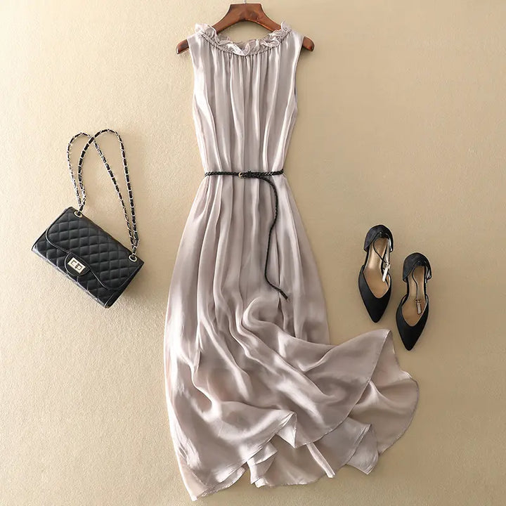 Muted grey pure silk midi slip dress laid flat with a black quilted handbag and black heels, featuring a ruffled neckline and braided belt.