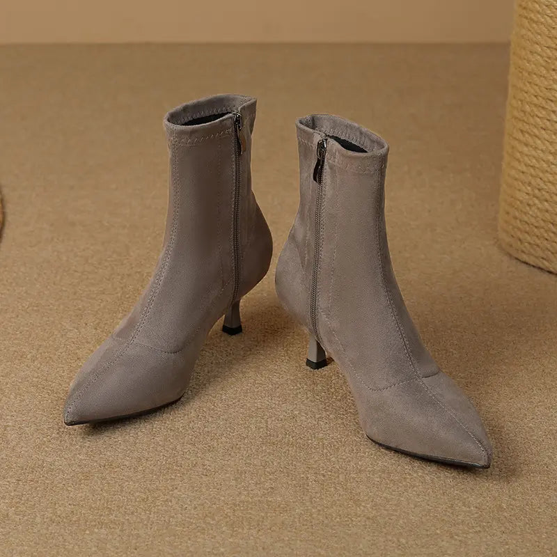 Grey suede-like stiletto ankle boots with a pointed toe and inner side zipper, presented in a three-quarter view on a textured background.