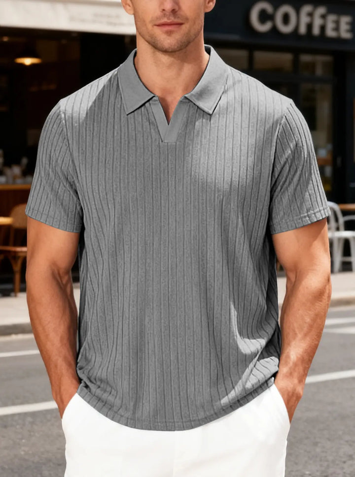 A man wears a grey textured knit V-neck polo shirt with short sleeves and fine vertical ribbing, styled casually on a street.