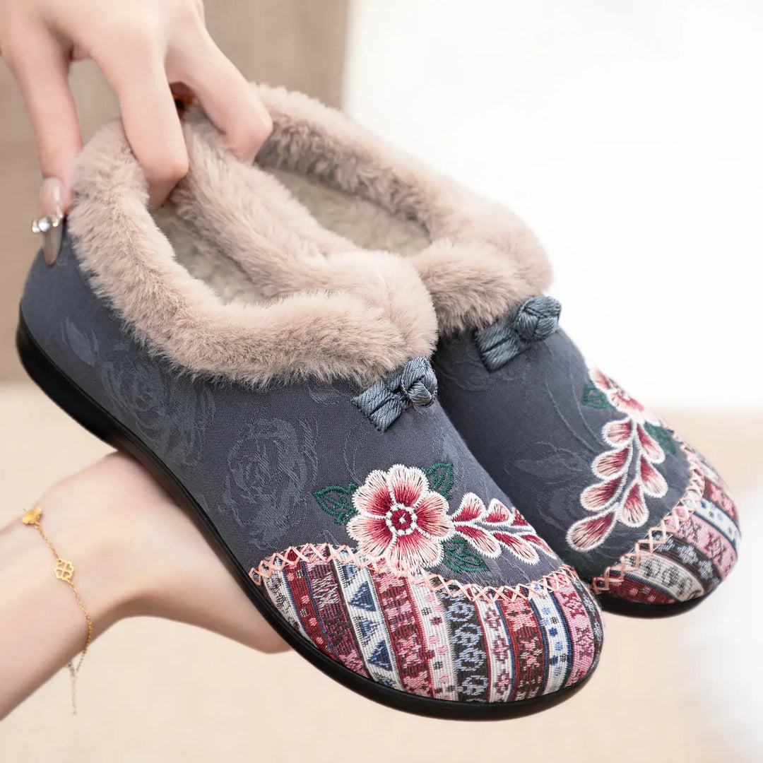 Grivan embroidered mules slippers in charcoal grey, featuring plush faux-fur lining, intricate floral embroidery, and a decorative bow accent, shown with a three-quarter view.