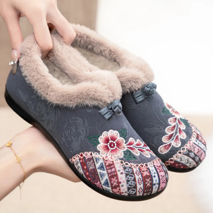 Grivan embroidered mules slippers in charcoal grey, featuring plush faux-fur lining, intricate floral embroidery, and a decorative bow accent, shown with a three-quarter view.