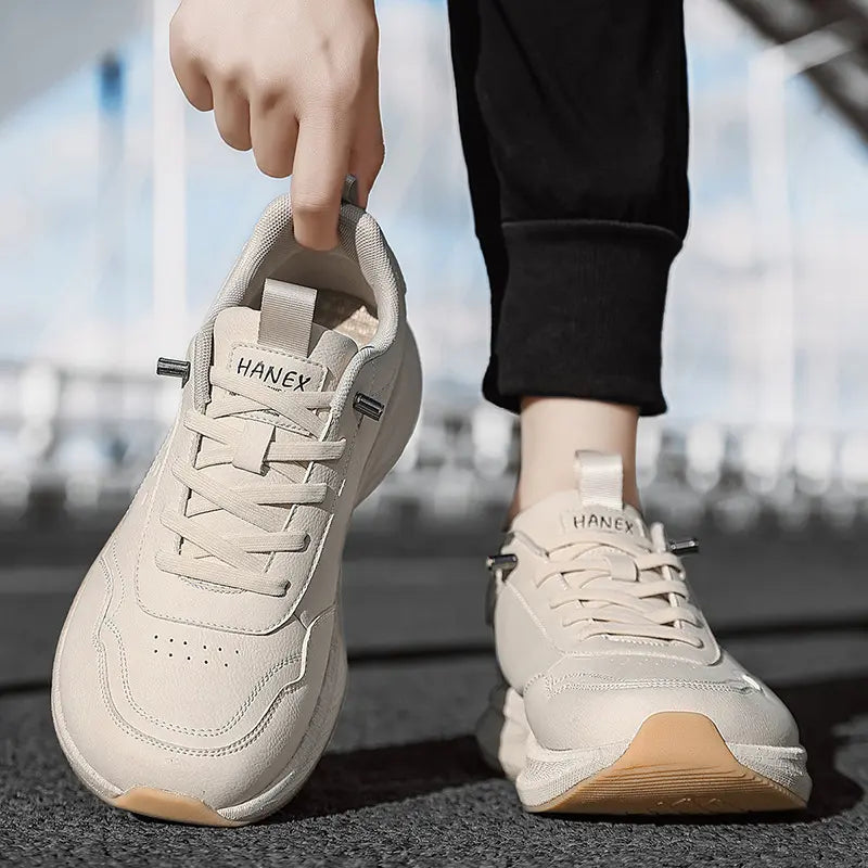 Pair of light beige wide-fit athletic trainers by HANEX, featuring a breathable mesh upper, lace-up closure, and a chunky white EVA midsole with a contrasting brown rubber outsole, shown from a three-quarter angle.