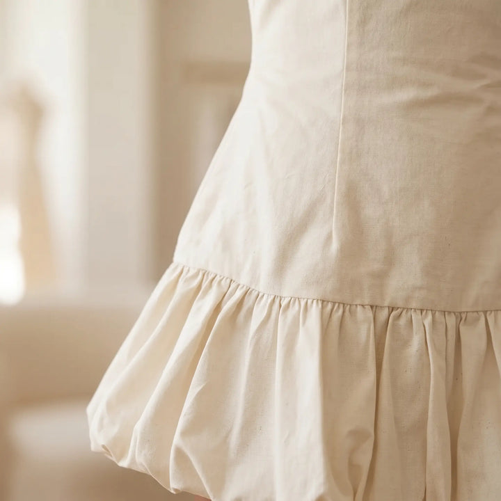 Close-up of a creamy ivory sleeveless dress showing the textured cotton-linen blend fabric and the gathered micro-pleated ruffle hem detail.