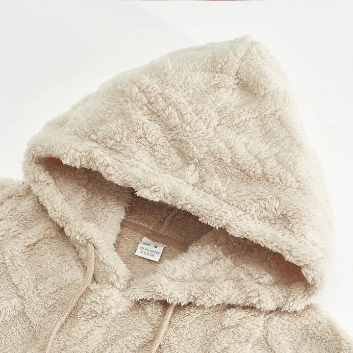 Close-up view of a textured ivory fleece hoodie, showcasing the plush fabric, adjustable drawstring hood, and interior size label.
