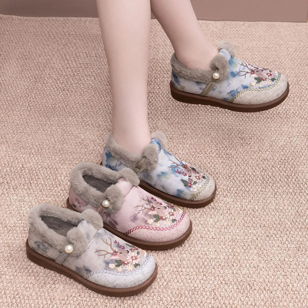 Jevok embroidered plush slippers in dusty rose, warm grey, and muted sage patterns, featuring faux fur trim and pearl accents, shown on feet with a textured carpet background.