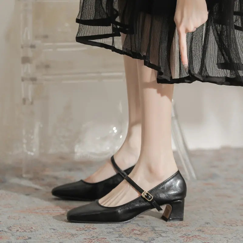 Black Kaelan Mary Jane block heel pumps with a square toe and single buckle strap, worn by a model in a chic lifestyle setting.