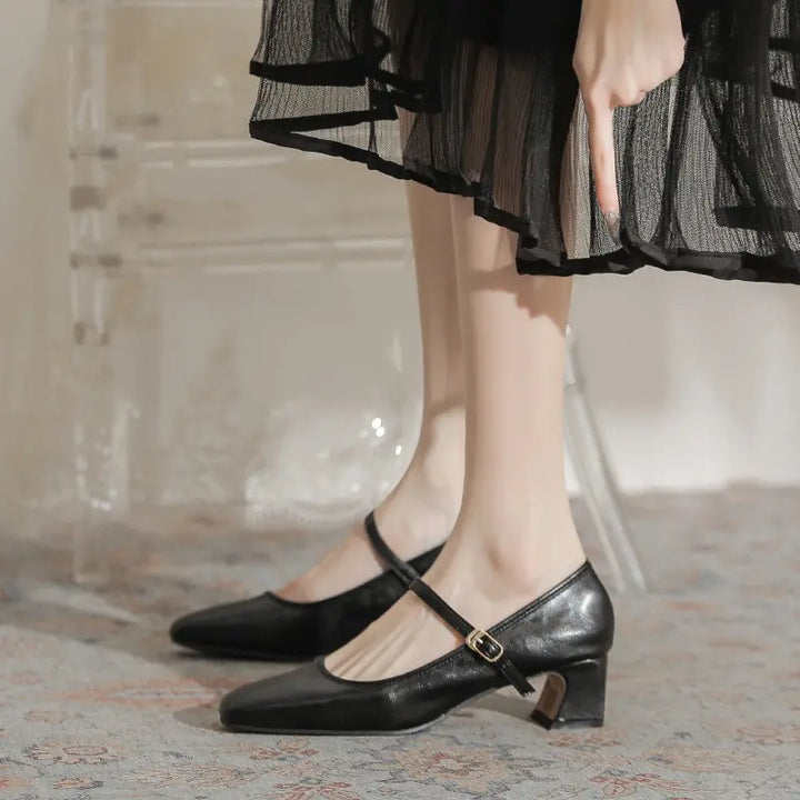 Black Kaelan Mary Jane block heel pumps with a square toe and single buckle strap, worn by a model in a chic lifestyle setting.
