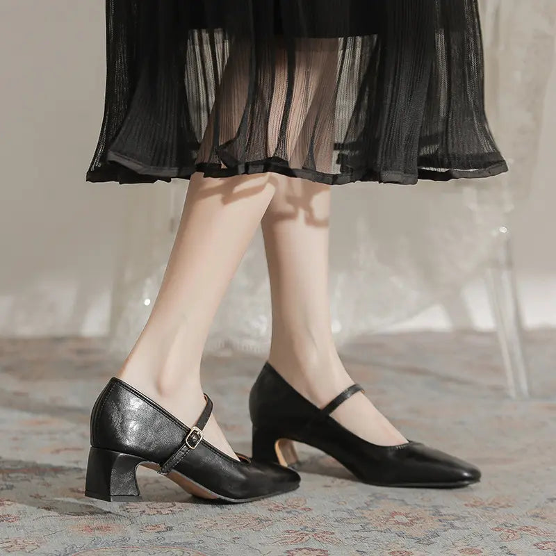Black Kaelan Mary Jane block heel shoes with square toe and gold buckle strap, worn by a woman in a sophisticated setting with a sheer black dress.