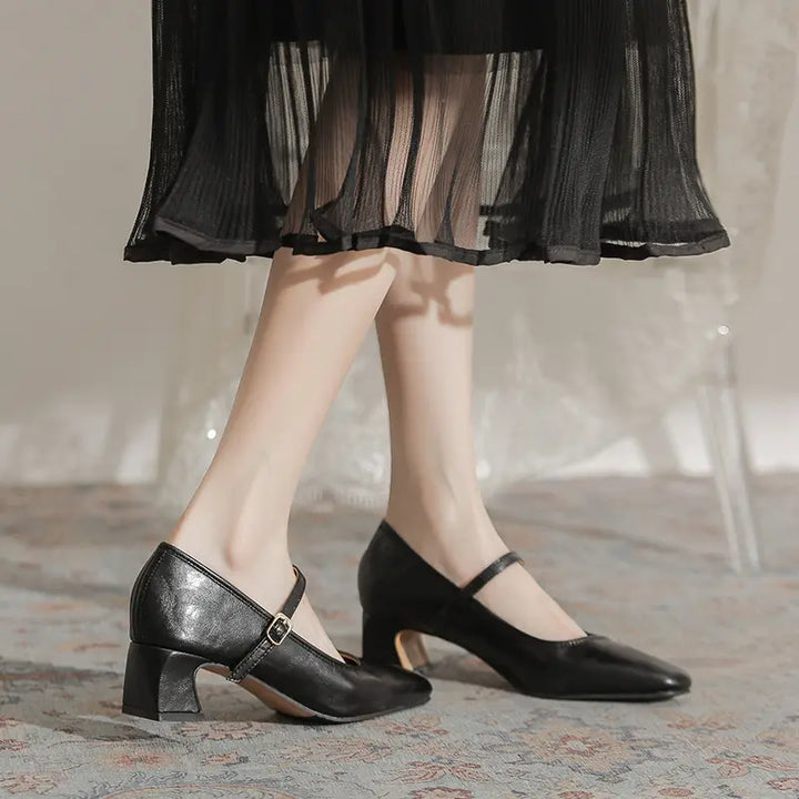 Black Kaelan Mary Jane block heel shoes with square toe and gold buckle strap, worn by a woman in a sophisticated setting with a sheer black dress.