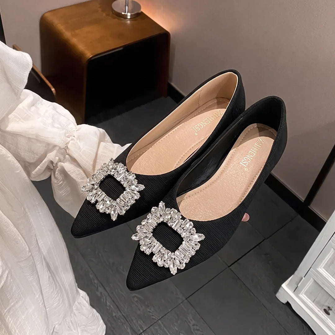 Pair of black Kaelan pointed-toe flat shoes adorned with a dazzling square rhinestone buckle embellishment on the vamp, showcasing their ribbed texture and elegant profile.