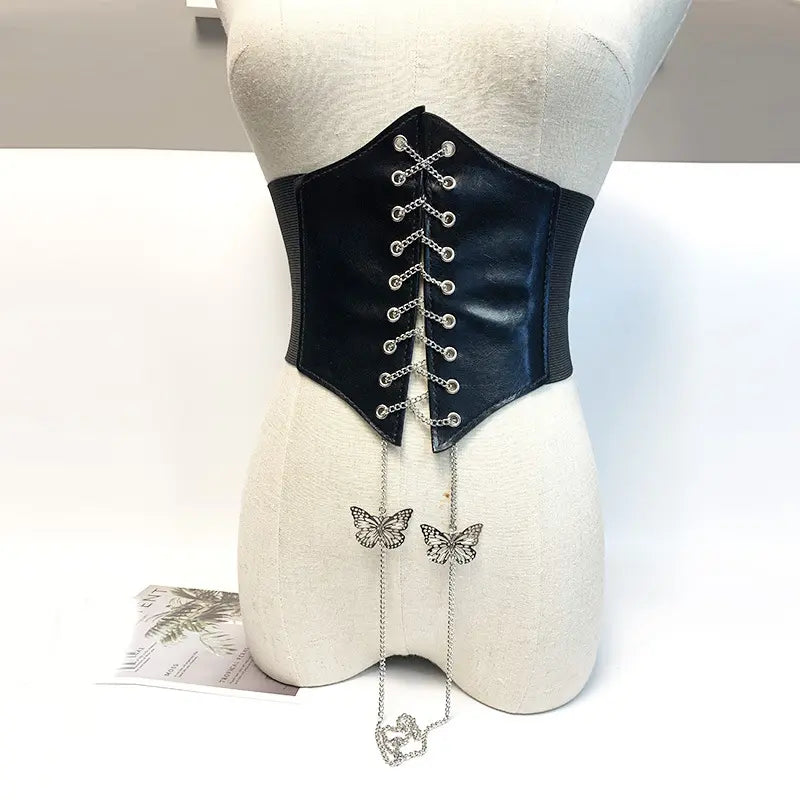 Black wide corset belt with silver chain lacing and detailed butterfly charms, displayed on a mannequin against a white studio background.