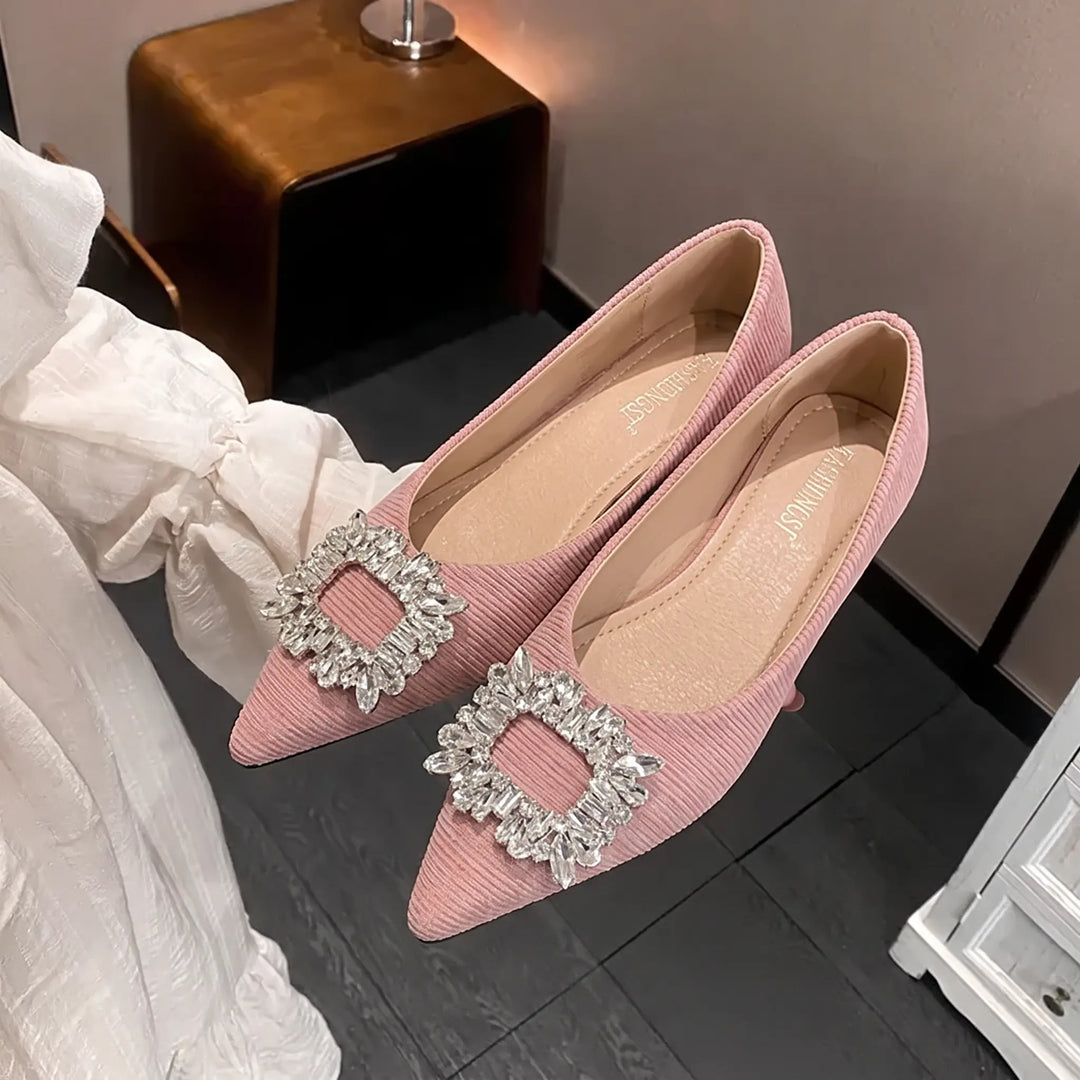 Dusty rose pink pointed-toe flats adorned with a large square rhinestone buckle embellishment, featuring a ribbed upper texture. Elegant slip-on women&