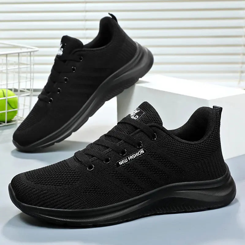 Black Kaelen breathable mesh trainers for running and everyday comfort, shown from a three-quarter front angle with a second shoe visible behind. Features tonal laces and a subtle 'NEW FASHION' side label.