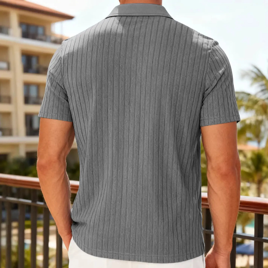 Kaelen men's grey textured knit short-sleeve polo shirt, shown from the back in a casual lifestyle setting with a resort-style building and palm trees.