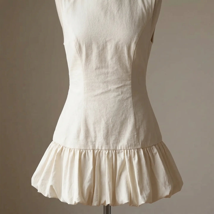 Creamy ivory sleeveless mini dress featuring a fitted bodice and a voluminous, micro-pleated ruffle hem with a wavy edge. Textured cotton blend fabric.