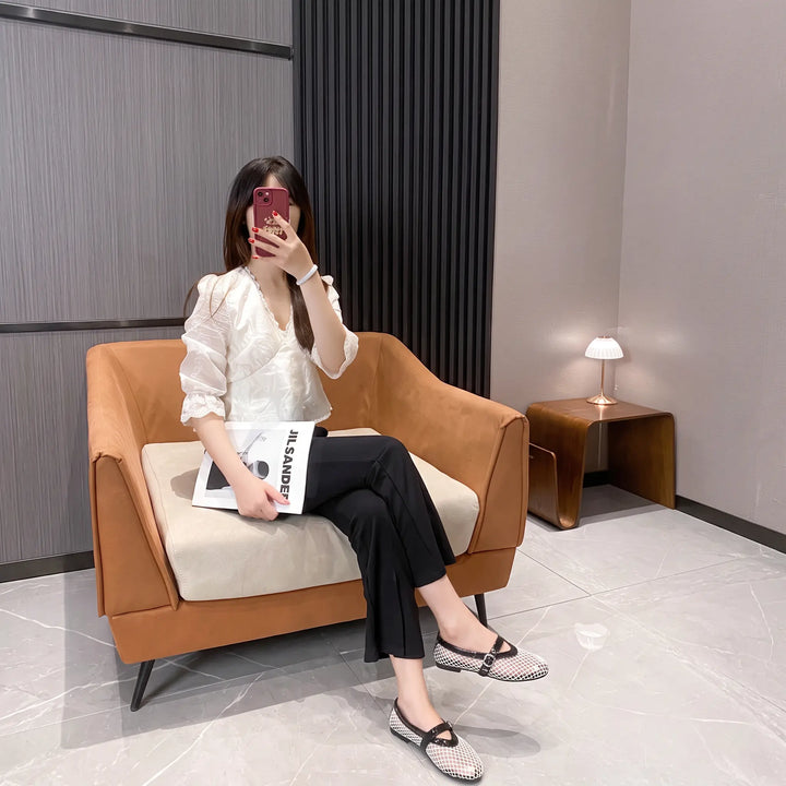 Lifestyle image of Kaelen mesh ballet flats with a patent Mary Jane strap worn by a woman sitting on a chair, showcasing their elegant design and comfortable fit.