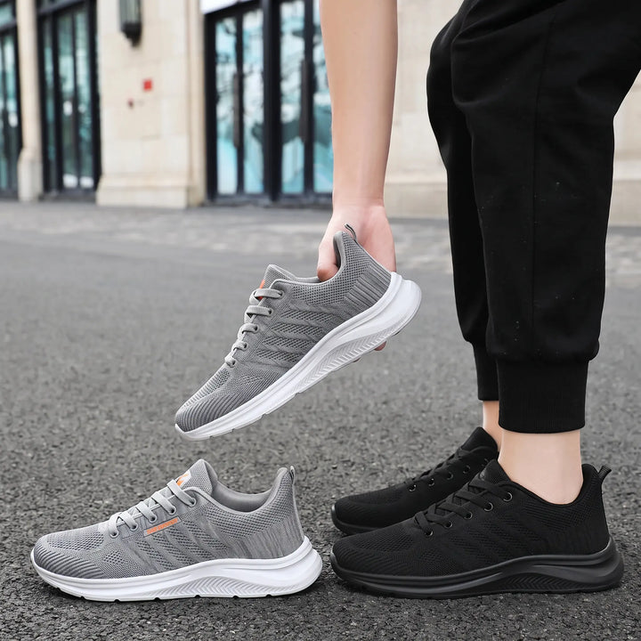 Lifestyle shot showcasing Kaelen breathable mesh trainers in grey and black, held and displayed on a street background. The shoes feature a lightweight design and modern athletic silhouette.