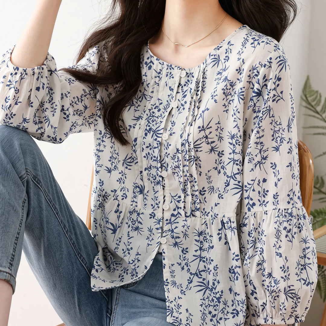 Woman wearing a white Kaelen floral print cotton puff sleeve blouse with blue motifs, round neckline, and three-quarter length sleeves, styled with jeans.