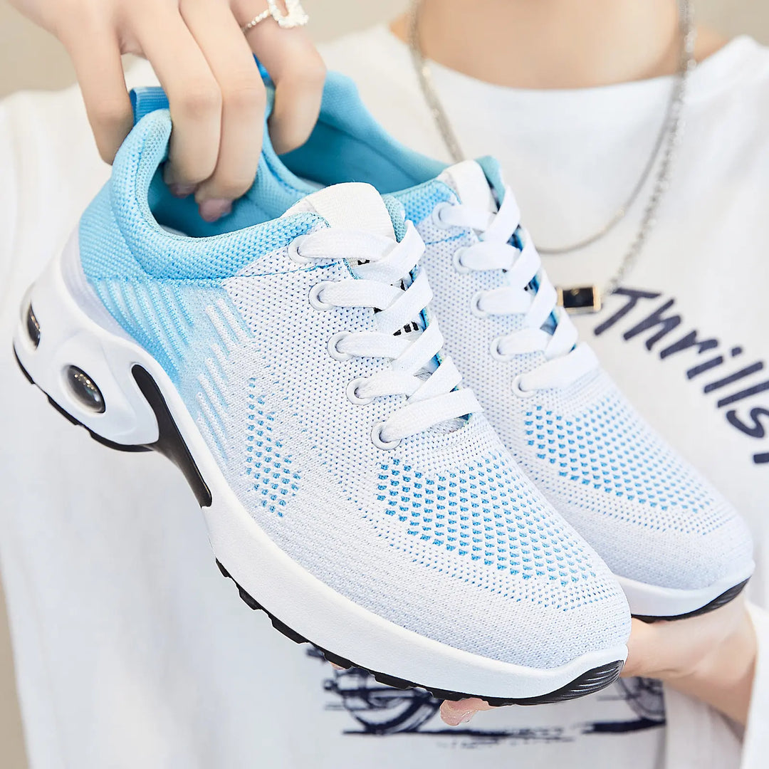 Pair of Kaelix breathable knit trainers in white with light blue abstract stripes, featuring white laces and a visible air cushioning sole, held by hands.