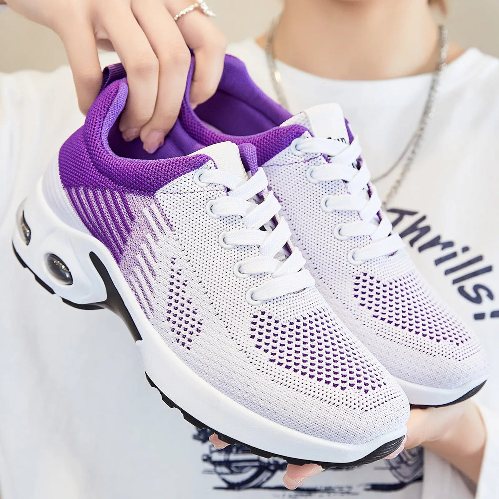 Pair of Kaelix breathable knit trainers in white with vibrant purple accents, shown from a three-quarter view held by a person.