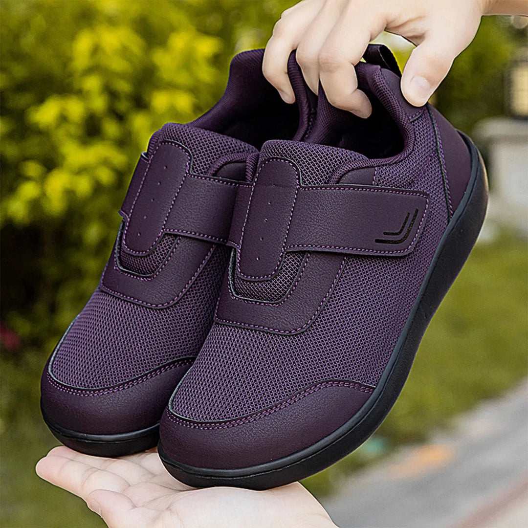 Pair of Kaelo purple breathable mesh walking shoes with dual hook-and-loop straps, shown from a three-quarter angle with a blurred green foliage background.