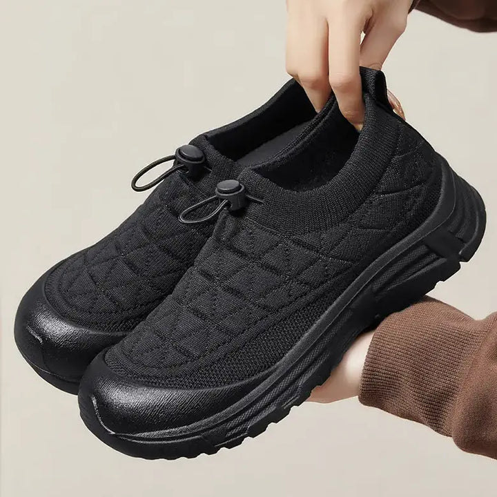 Black quilted knit slip-on sneakers with a cream rubber toe cap and bungee laces, shown from a three-quarter angle.
