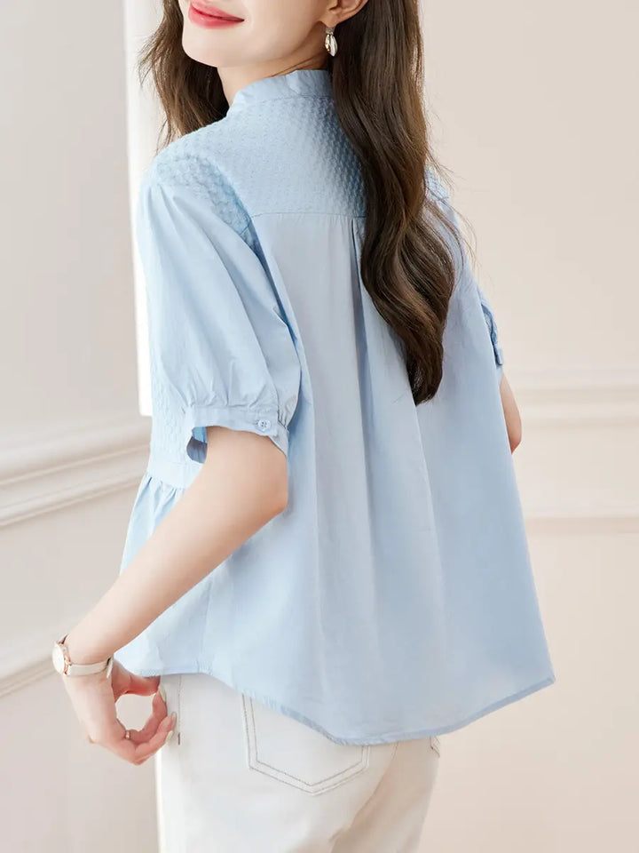 Kaelos light blue cotton peplum blouse with woven chest panel, mandarin collar, and short puff sleeves, shown from the side view.