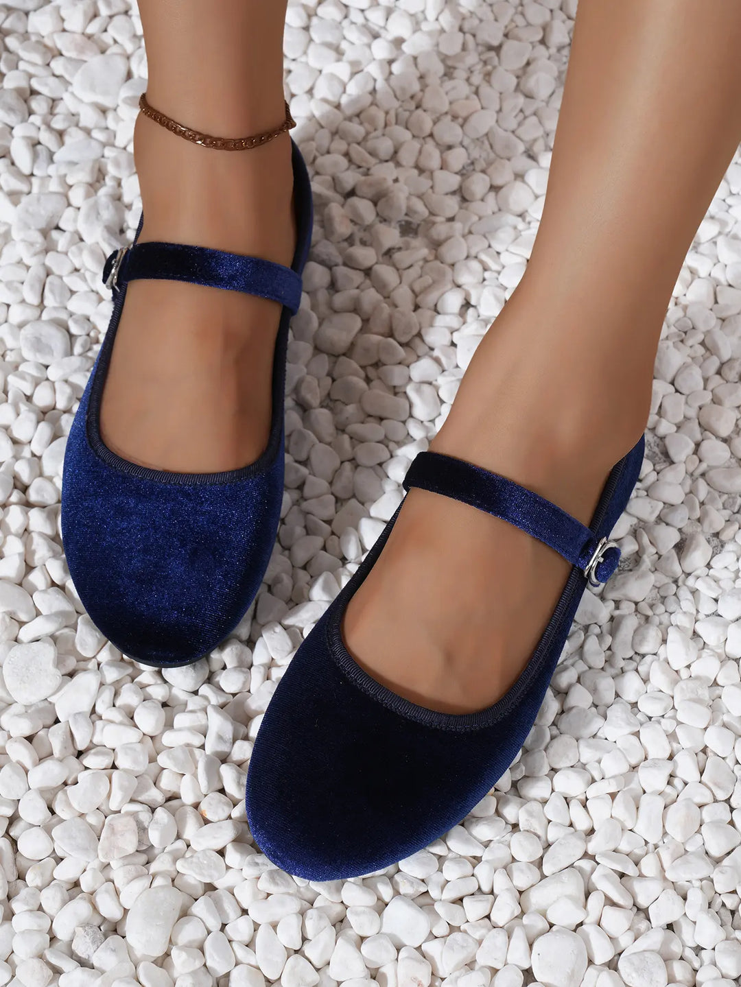 Kaelos sapphire velvet Mary Jane ballet flats featuring a round toe and an adjustable silver buckle strap, shown on feet with an anklet on a white pebble background.