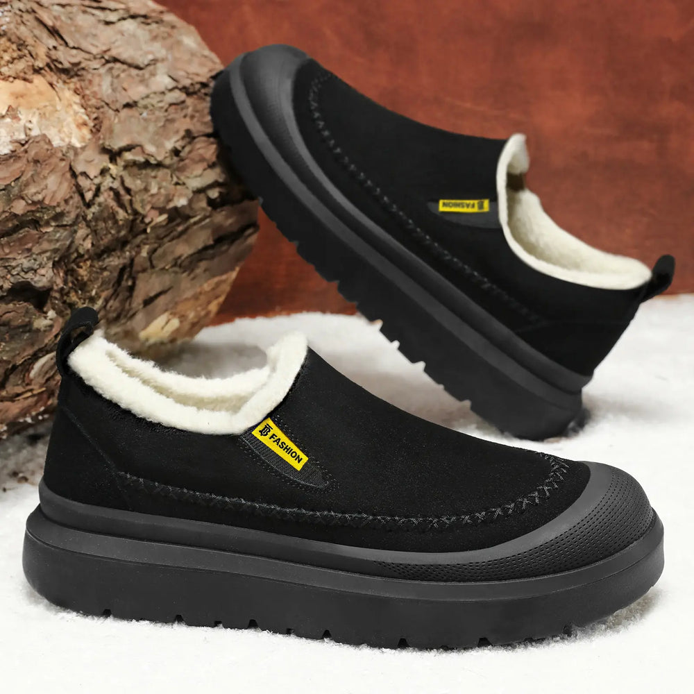 Black men's slip-on winter boots with plush faux fur lining and a decorative stitching detail on the vamp, resting on a white surface with a wood element.