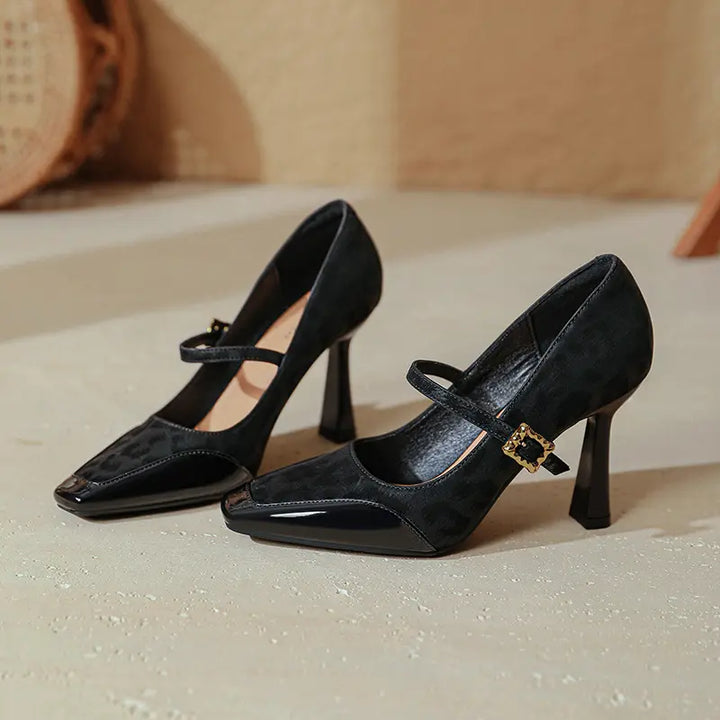 Black suede Mary Jane heels with patent leather toe caps and accents, featuring a subtle leopard print and a decorative gold-tone buckle strap.