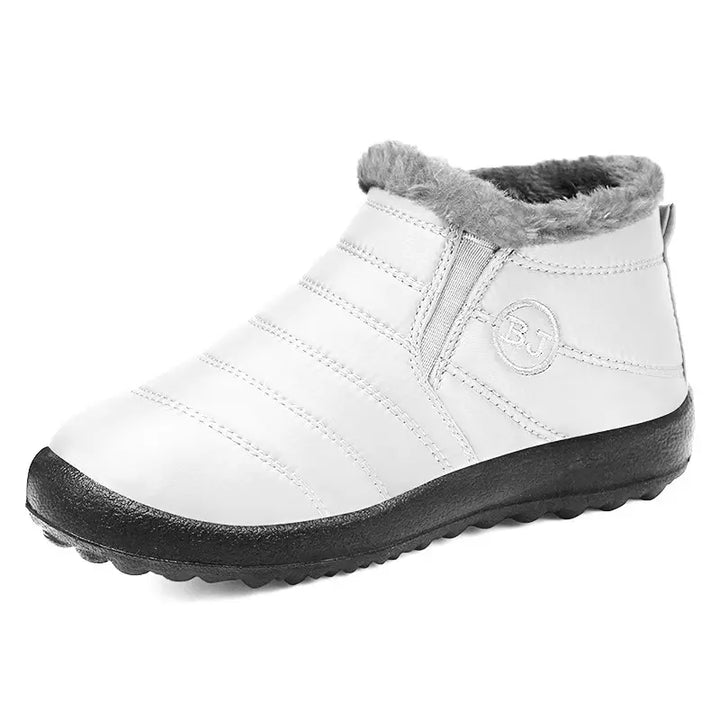 White Kaelum winter ankle boots for women and men, featuring a quilted water-resistant upper, plush grey faux fur lining, and a flat black lugged sole. Easy slip-on design with elasticated side gussets.
