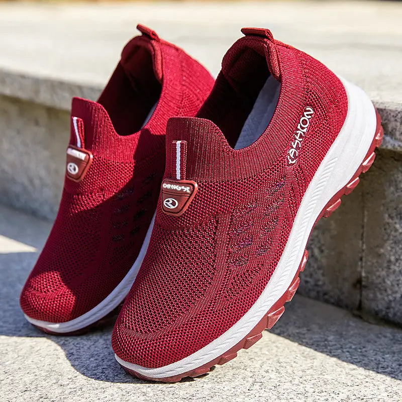 Crimson ruby red Kaelum women's breathable slip-on sneakers shown from a three-quarter angle, featuring a knitted mesh upper with subtle multi-colored thread accents and a white 'FASHION' graphic on the side.
