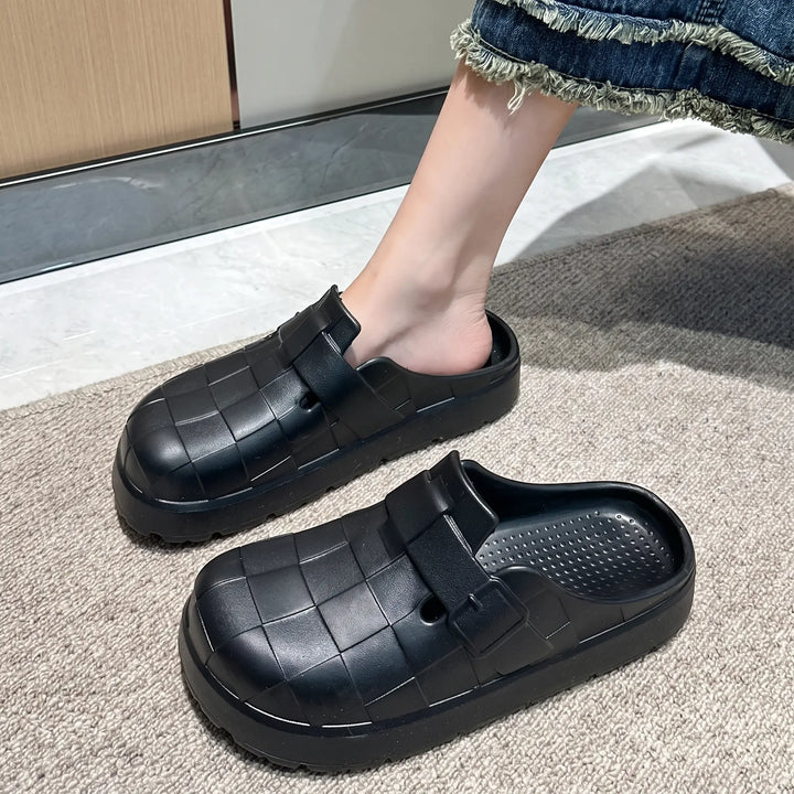 Black EVA clogs with a distinctive woven upper, worn by a person indoors, showcasing their soft, thick-soled design and waterproof comfort.